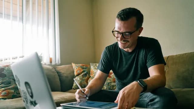 Designer sorrindo enquanto desenha em um tablet ao lado do notebook