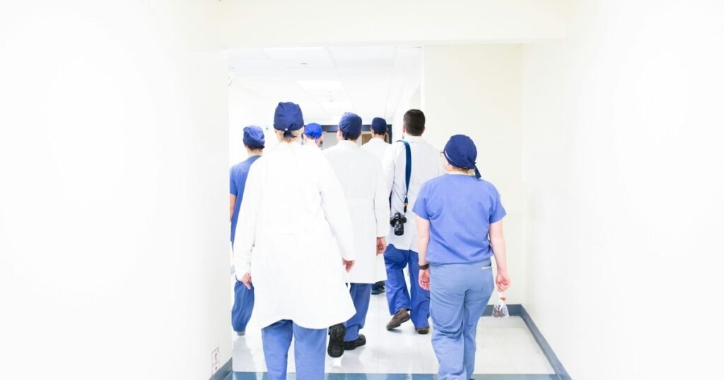 Equipe multiprofissional de saúde caminha por corredor claro de hospital