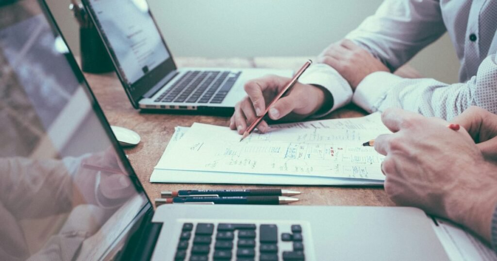 Dois profissionais analisam documento de planejamento sobre a mesa entre notebooks em escritório
