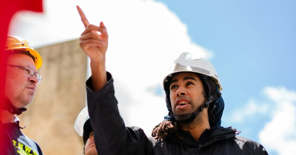 Engenheiro com capacete apontando e liderando equipe em obra, representando a transição para gestão em engenharia