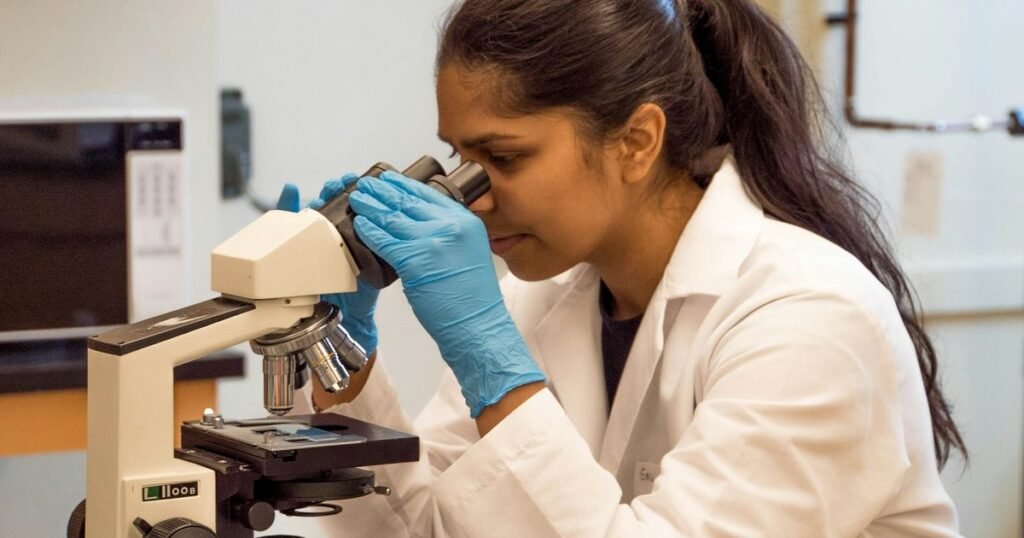 Biomédica analisando amostra em microscópio de laboratório