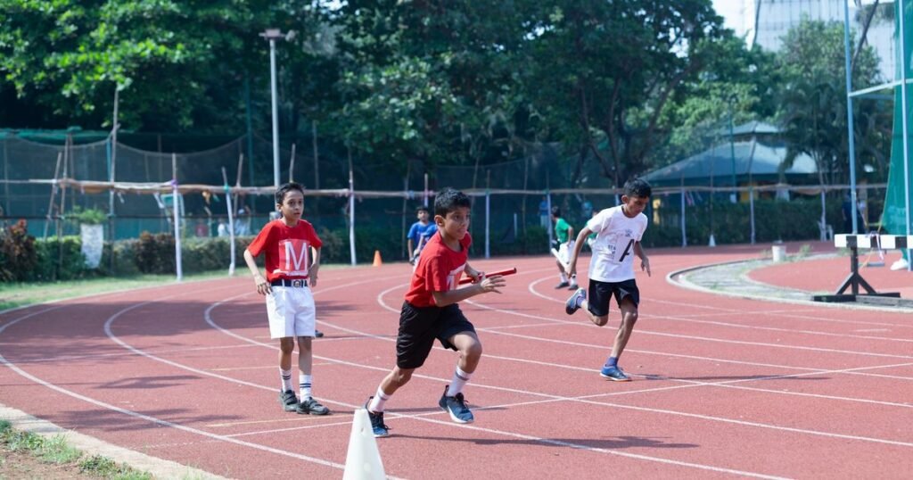 Alunos correm em revezamento numa pista de atletismo escolar durante aula de educação física