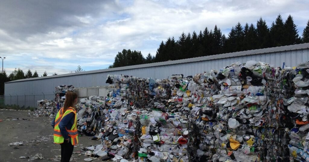 Profissional com colete de segurança observando fardos de material reciclado em centro de triagem de resíduos