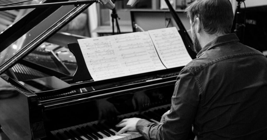 Músico ao piano lendo partitura de arranjo em estúdio de gravação